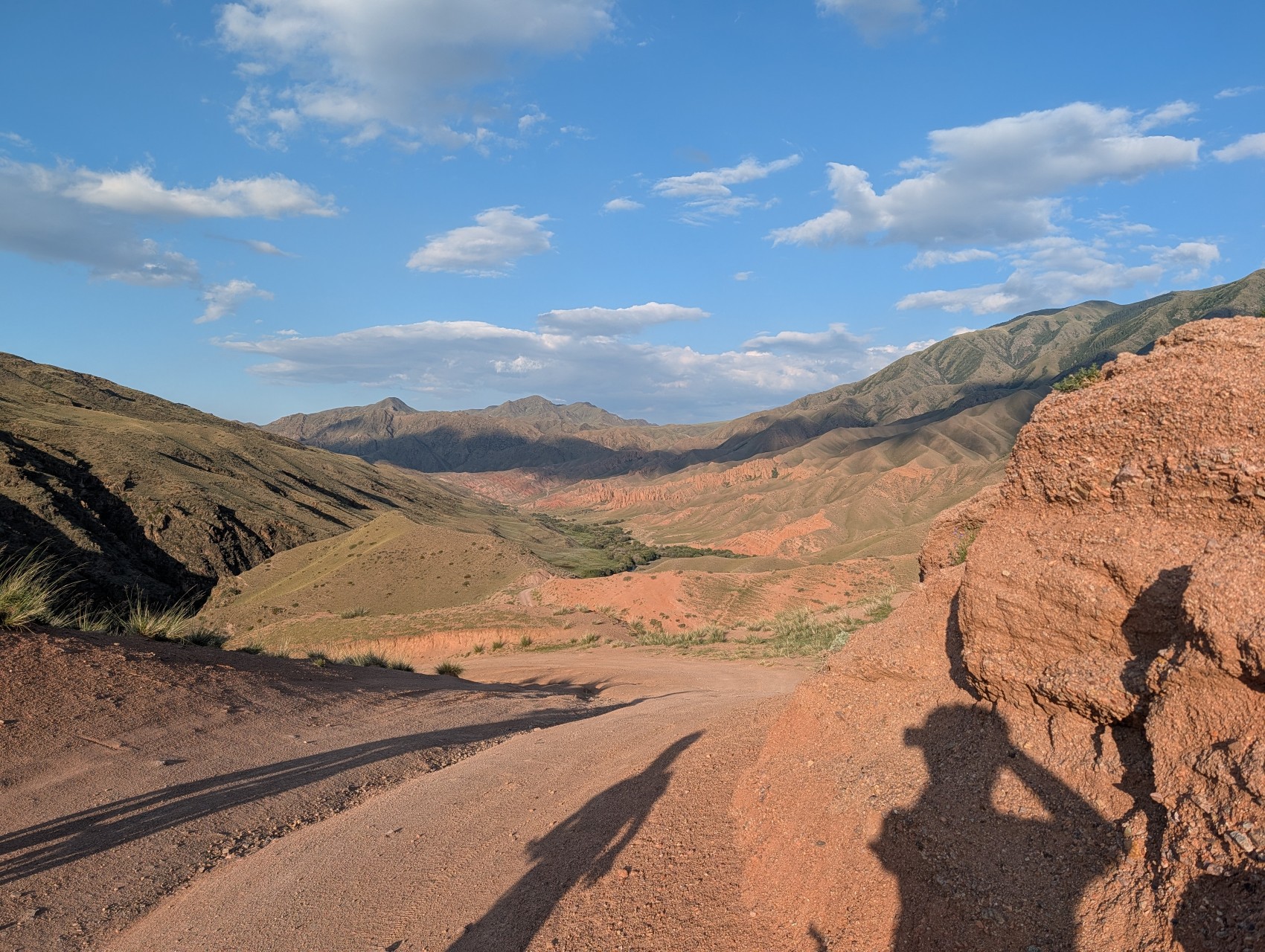 Red gravel road descending into a green valley